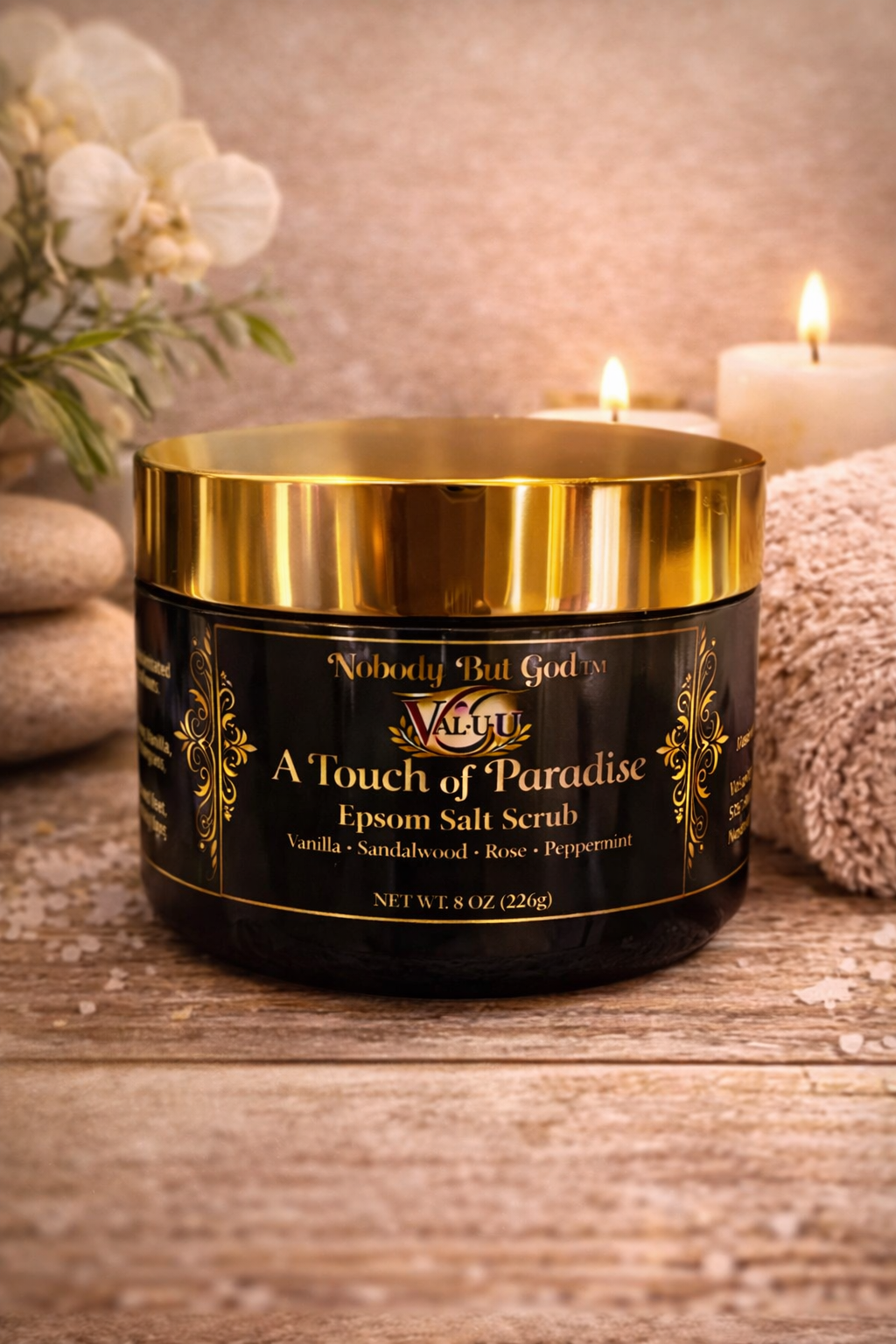 Black and gold jar of Epsom salt scrub on a wooden surface with candles and flowers in the background.