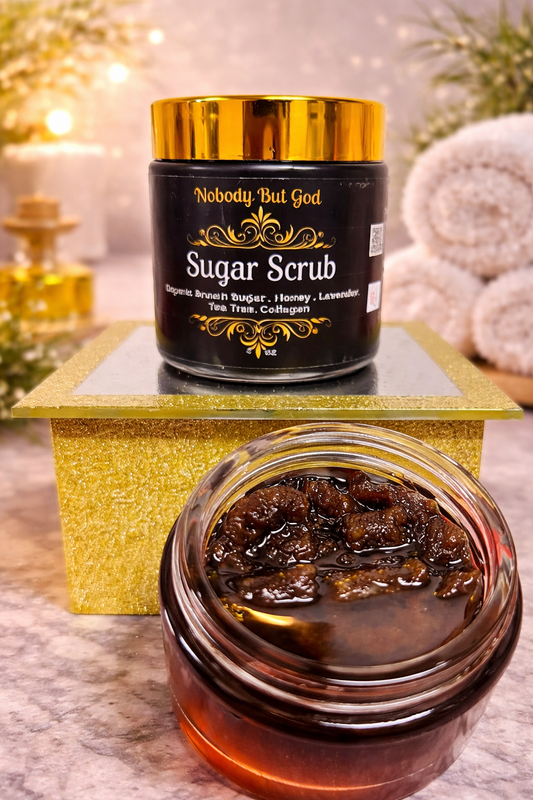 Jar of sugar scrub with gold lid on a decorative stand, surrounded by bath products.